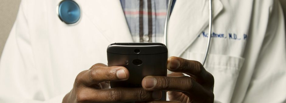 A clinician in a white coat reviewing patient messages on a phone
